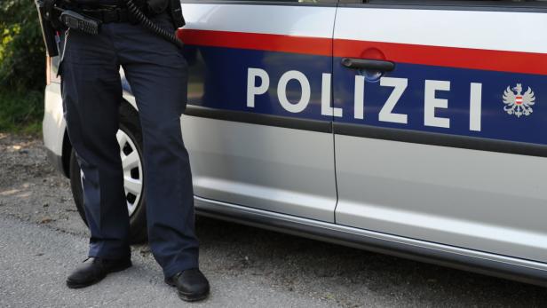 Ein Polizist steht neben einem Streifenwagen der österreichischen Polizei.