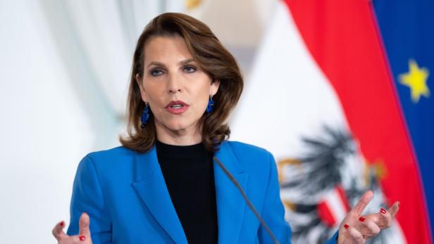 MINISTERRAT: EDTSTADLER Eine Frau in einem blauen Blazer spricht vor österreichischen und europäischen Flaggen.