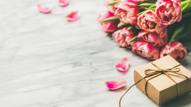 Ein Geschenk liegt neben einem Strauß rosa Tulpen auf einem Marmortisch.