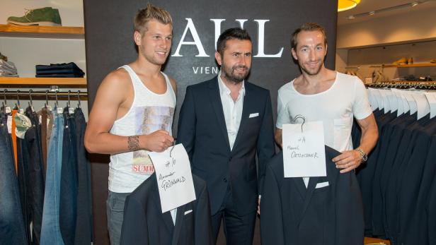 Alexander Grünwald, eine unbekannte Person und Manuel Ortlechner posieren mit Anzügen in einem Geschäft.