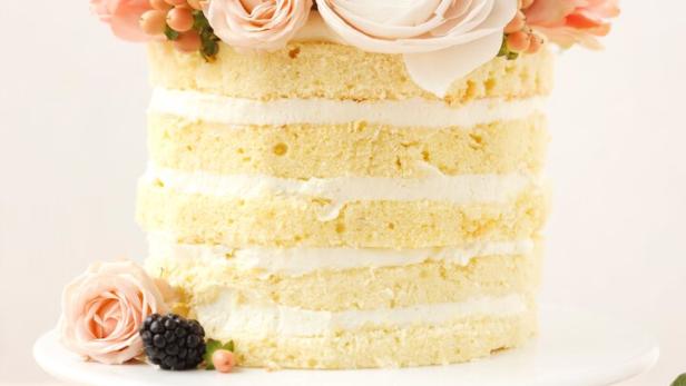 Ein Naked Cake mit Blumen und Brombeeren auf einem weißen Teller.