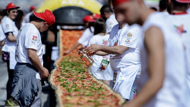 Neapolitan pizza makers attempt to make the longest pizza to break a Guinness World Record along the seafront of Naples, on May 18, 2016. For the wood-fired pizza, which measured two kilometres, they used 2,000 kg of flour, 1,600 kg of tomatoes, 2,000 kg of mozzarella, 200 litres of oil, 30kg of fresh basil. / AFP PHOTO / Mario LAPORTA