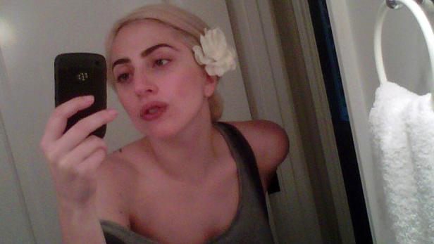 Eine Frau mit einer Blume im Haar macht ein Selfie mit ihrem Smartphone.