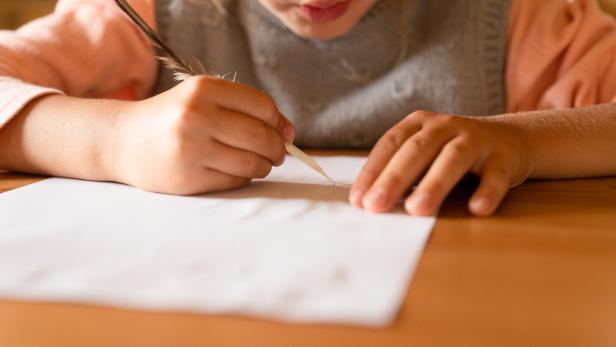 Ein Kind Schreibt auf einem Zettel etwas.