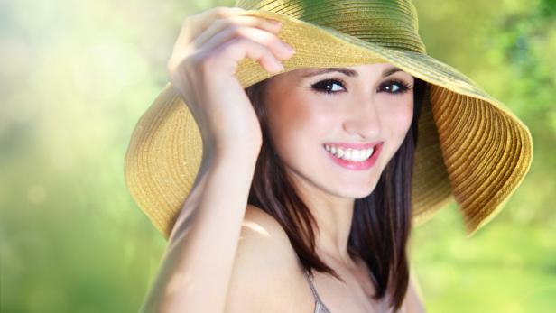 Eine lächelnde Frau mit braunen Haaren und einem großen Sonnenhut.