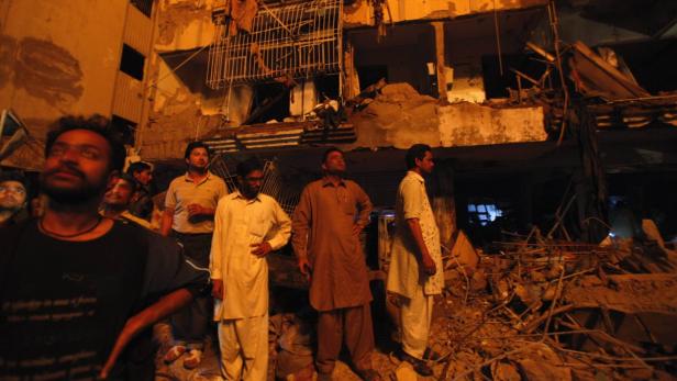 Residents stand in front of a damaged building after a bomb blast in a residential area in Karachi March 3, 2013. A bomb attack in a Shi&#039;ite Muslim area of Pakistan&#039;s commercial capital Karachi killed 25 people and wounded 50 on Sunday, the police said. REUTERS/Akhtar Soomro (PAKISTAN - Tags: CRIME LAW CIVIL UNREST POLITICS)