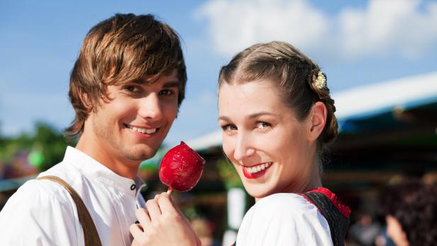 Ein Paar in Tracht hält gemeinsam einen roten Liebesapfel.