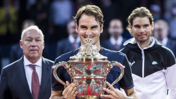 Roger Federer hält eine Trophäe, während Rafael Nadal im Hintergrund steht.