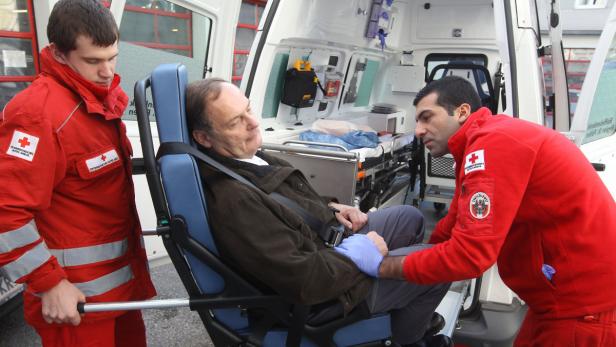 Rettungssanitäter schieben einen Patienten in einem Stuhl in einen Krankenwagen.