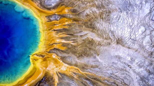 Luftaufnahme einer Thermalquelle mit blauem Wasser und gelben Ablagerungen.