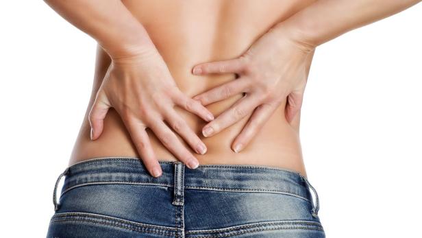 Eine Frau hält sich mit schmerzverzerrtem Gesicht den unteren Rücken.