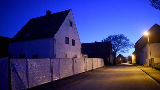 Eine ruhige Wohnstraße in der Dämmerung mit Häusern und Bauzäunen.