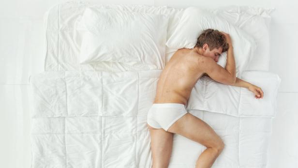 Ein Mann in Unterhose liegt in einem Bett und schläft.