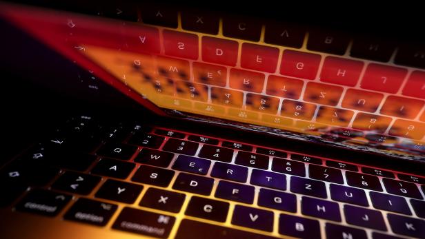 Eine beleuchtete Computertastatur spiegelt sich im Bildschirm, der in warmen Farben leuchtet.