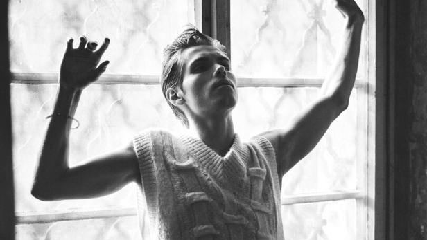 Ein Mann im ärmellosen Pullover sitzt am Fenster.