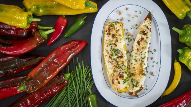 Gefüllte Paprika auf weißem Teller mit roten und gelben Paprikas und Schnittlauch rundherum