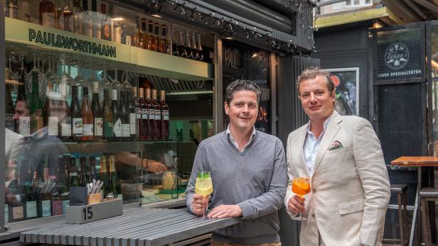 Zwei Männer stehen vor der Bar „Paul & Worthmann“ und halten Aperol Spritz in der Hand.