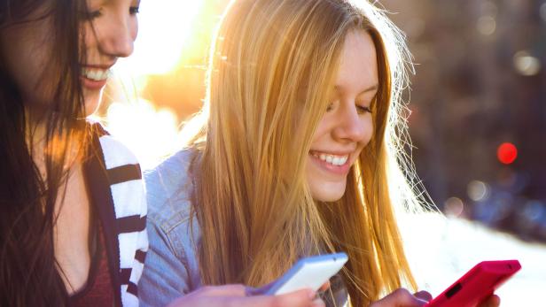 Zwei Teenager sind glücklich mit ihrem Handy in der Hand.