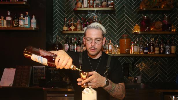 Ein Barkeeper mit Tätowierungen mixt einen Cocktail in einer Bar.