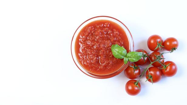 Eine Schüssel mit Tomatensauce, garniert mit Basilikum, neben einem Zweig Kirschtomaten.