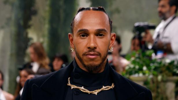 Lewis Hamilton trägt ein schwarzes Outfit mit goldenen Schmuckdetails.