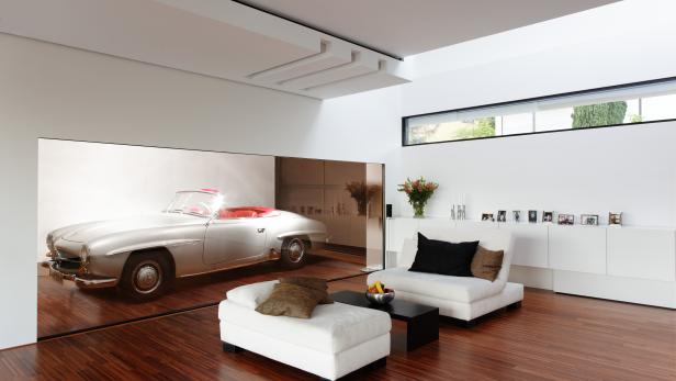Ein Wohnzimmer mit weißen Möbeln und einem Oldtimer-Mercedes im Hintergrund.
