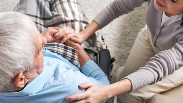 Young supportive female caregiver sitting by senior man in wheelchair