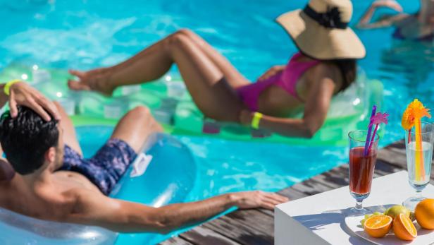 Menschen entspannen sich mit Getränken auf Schwimmreifen in einem Pool.