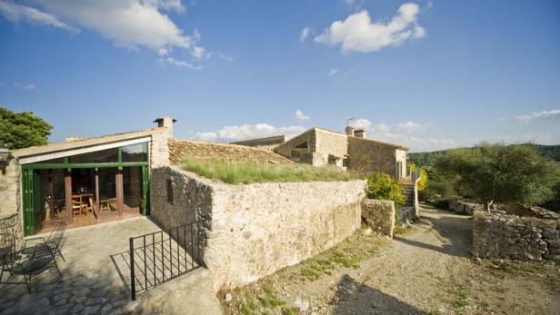Ein Landhaus mit Steinfassade und begrüntem Dach unter blauem Himmel.