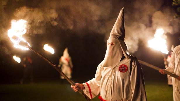 Personen in Ku-Klux-Klan-Gewändern halten brennende Fackeln in der Nacht.