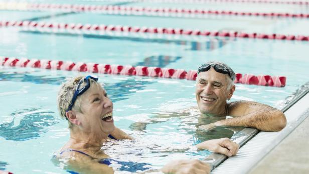 Ein älterer Mann und eine ältere Frau lehnen im Schwimmbecken am Rand.