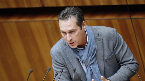 Ein Mann mit grauem Sakko und blauem Schal spricht vor Mikrofonen.