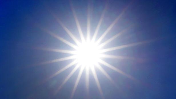 Helle Sonne strahlt mit Lichtstrahlen vor blauem Himmel.