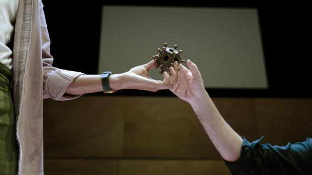 Eine hand reicht ein Objekt, einen römischen Dodekaeder, an eine andere Hand weiter