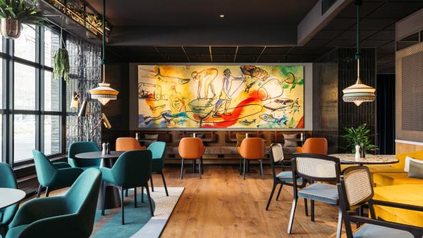 Ein Innenraum mit farbenfrohen Stühlen und einem großen, abstrakten Gemälde an der Wand.