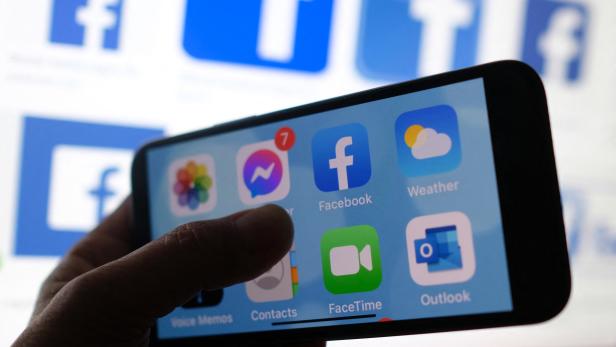 Eine Hand hält ein Smartphone mit geöffnetem Startbildschirm, auf dem verschiedene App-Symbole wie Facebook und Messenger zu sehen sind.