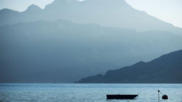 Nebelige Berglandschaft hinter dem Attersee im Salzkammergut, ein Boot im See 