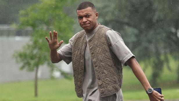 Fußballer Kylian Mbappé auf dem Weg zum Trainingslager in einer stylischen, beigen Weste.