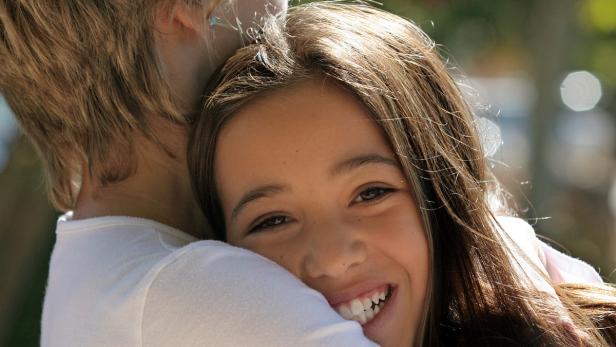 Ein lächelndes Mädchen umarmt eine Person.