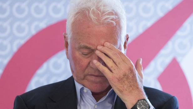Ein Mann mit weißem Haar hält seine Hand an seine Stirn.