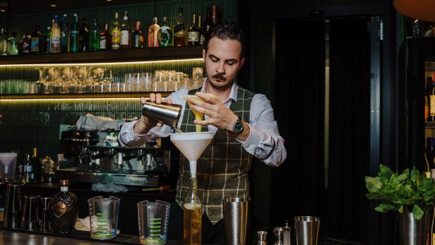 Ein Barkeeper mixt einen Cocktail hinter der Bar.