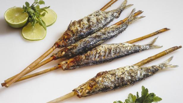 Gegrillte Sardinen am Spieß, garniert mit Limetten und Kräutern.