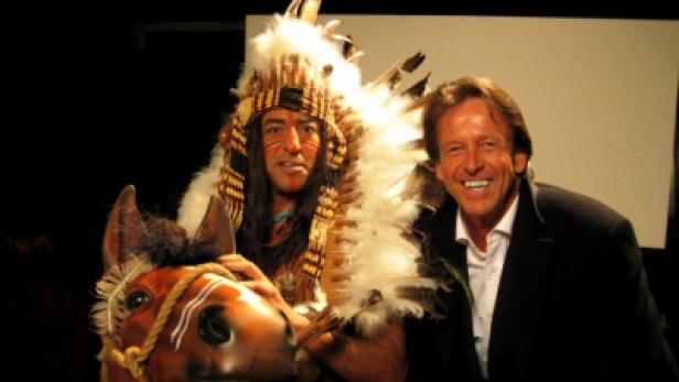 Ein Mann im Indianerkostüm posiert mit einem Mann im Anzug vor einem dunklen Hintergrund.