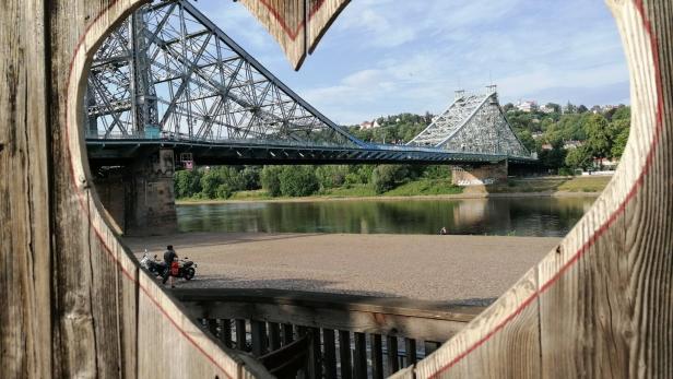 Blick durch einen Holzrahmen in Herzform auf die Brücke "Blaues Wunder" in Dresden