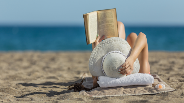 Frau liest am Strand ein Buch.