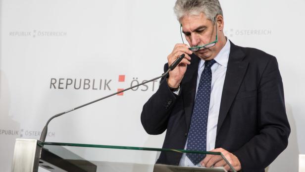 Ein Mann mit Brille steht an einem Rednerpult vor dem Hintergrund „Republik Österreich“.