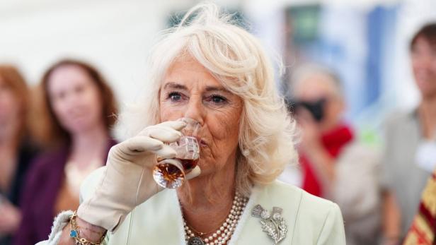 Queen Camilla trink aus einem kleinen Glas.