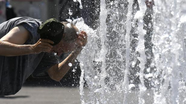 Ein Mann erfrischt sich an einem heißen Tag an einem Springbrunnen.