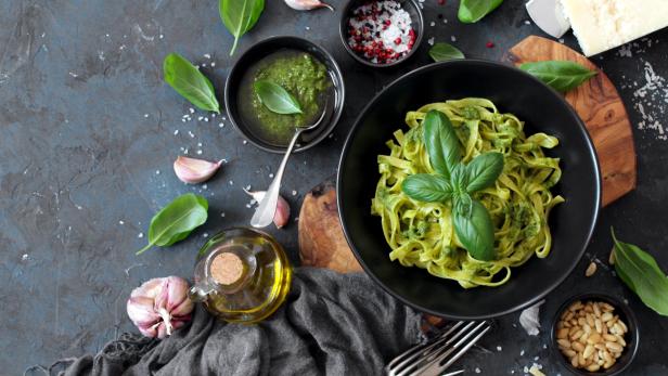 Pasta-Tagliatelle mit Pesto und frischen Basilikumblättern in einer schwarzen Schüssel.