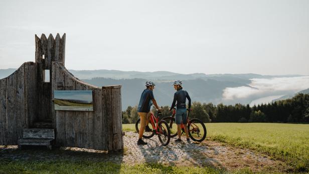 Zwei Radfahrer machen eine Pause an einem Aussichtspunkt mit Blick auf die Landschaft.